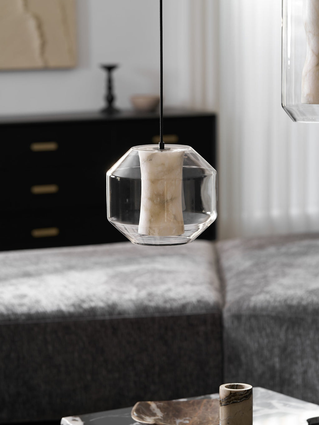 A wide Clérachic pendant with an unlit alabaster column hangs above a grey sofa, with a dark cabinet and a pale artwork behind it.