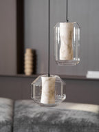 Two unlit Clérachic pendants, a tall one above a wide one, in front of a dark shelf with a ribbed brown vase, with grey seating below.