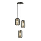 Three tall smoke grey glass Clérachic pendants hang at staggered heights from a round black canopy on a white backdrop.
