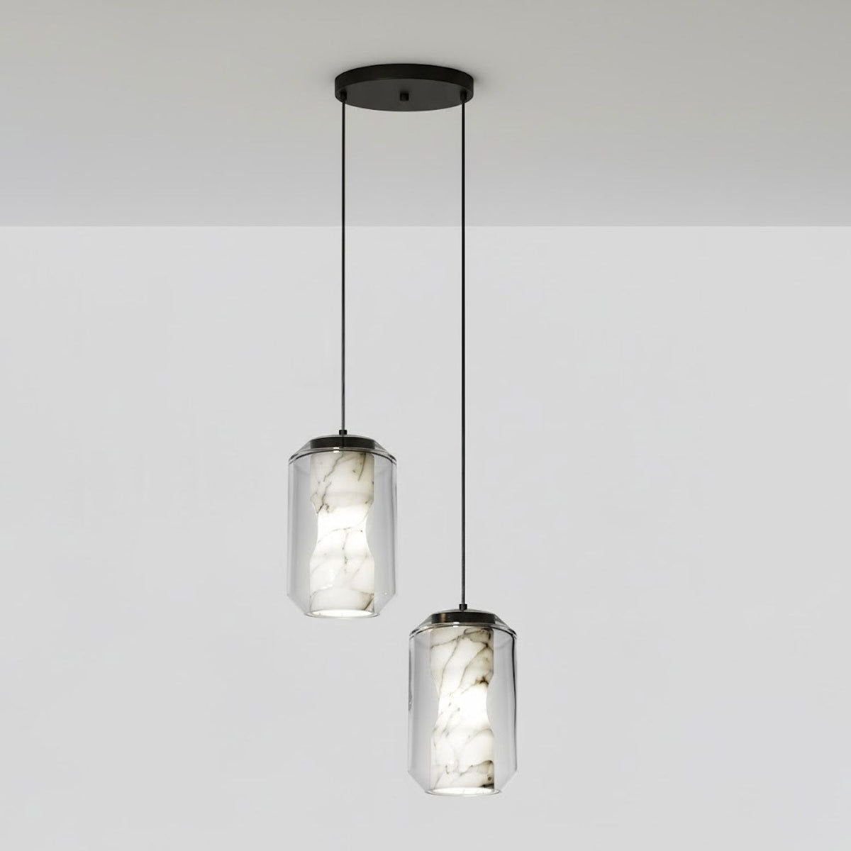 Two tall clear glass Clérachic pendants with veined alabaster hang at different drops from a round black canopy against a pale grey wall.