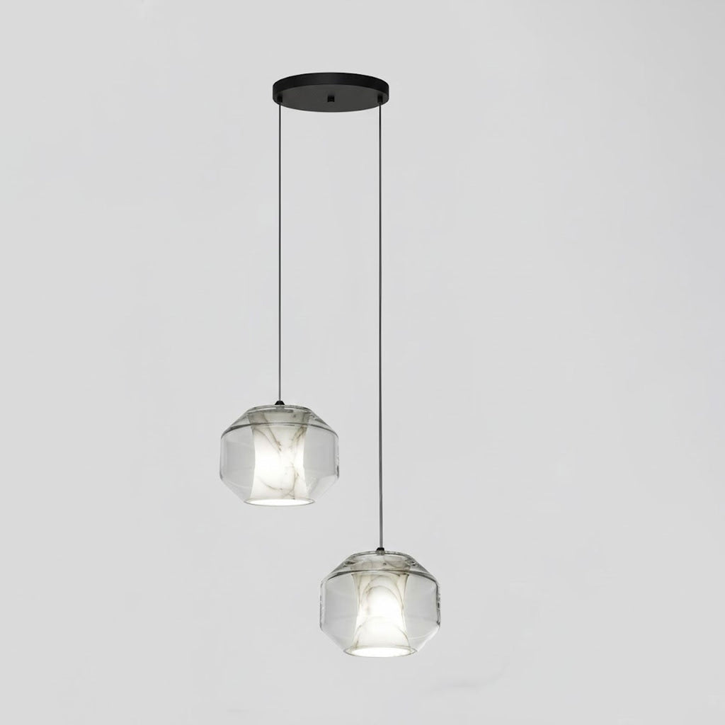 Two wide clear glass Clérachic pendants with white alabaster hang at different heights from a black canopy against a pale grey wall.