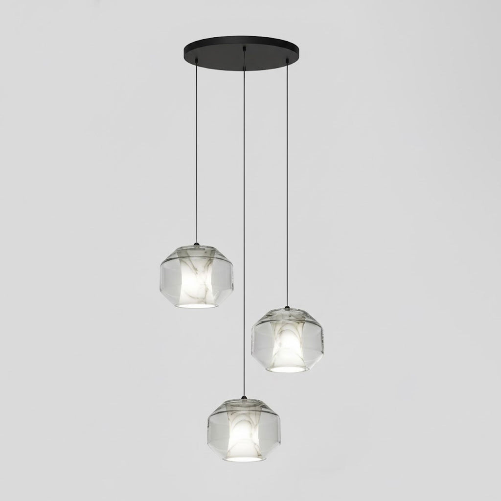 Three wide clear glass Clérachic pendants hang at staggered heights from a round black canopy against a pale grey wall.