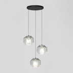 Three wide clear glass Clérachic pendants hang at staggered heights from a round black canopy against a pale grey wall.