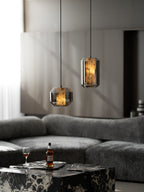 Two smoke grey Clérachic pendants glowing amber over a marble table with a whisky bottle and glass, in front of a grey sofa.