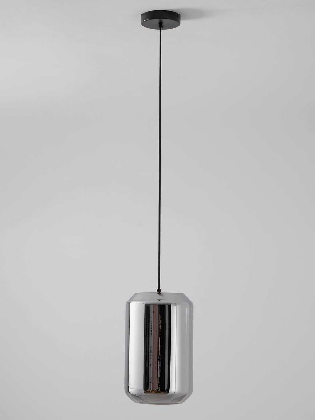 A tall Clérachic pendant with a mirrored smoke grey glass shell hangs on a black cord and canopy against a pale grey wall, unlit.