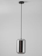 A tall Clérachic pendant with a mirrored smoke grey glass shell hangs on a black cord and canopy against a pale grey wall, unlit.