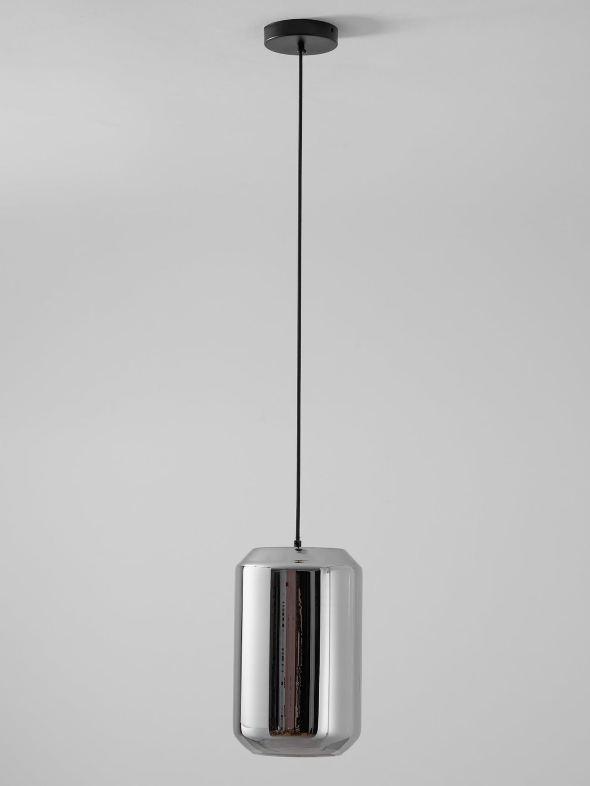 A tall Clérachic pendant with a mirrored smoke grey glass shell hangs on a black cord and canopy against a pale grey wall, unlit.