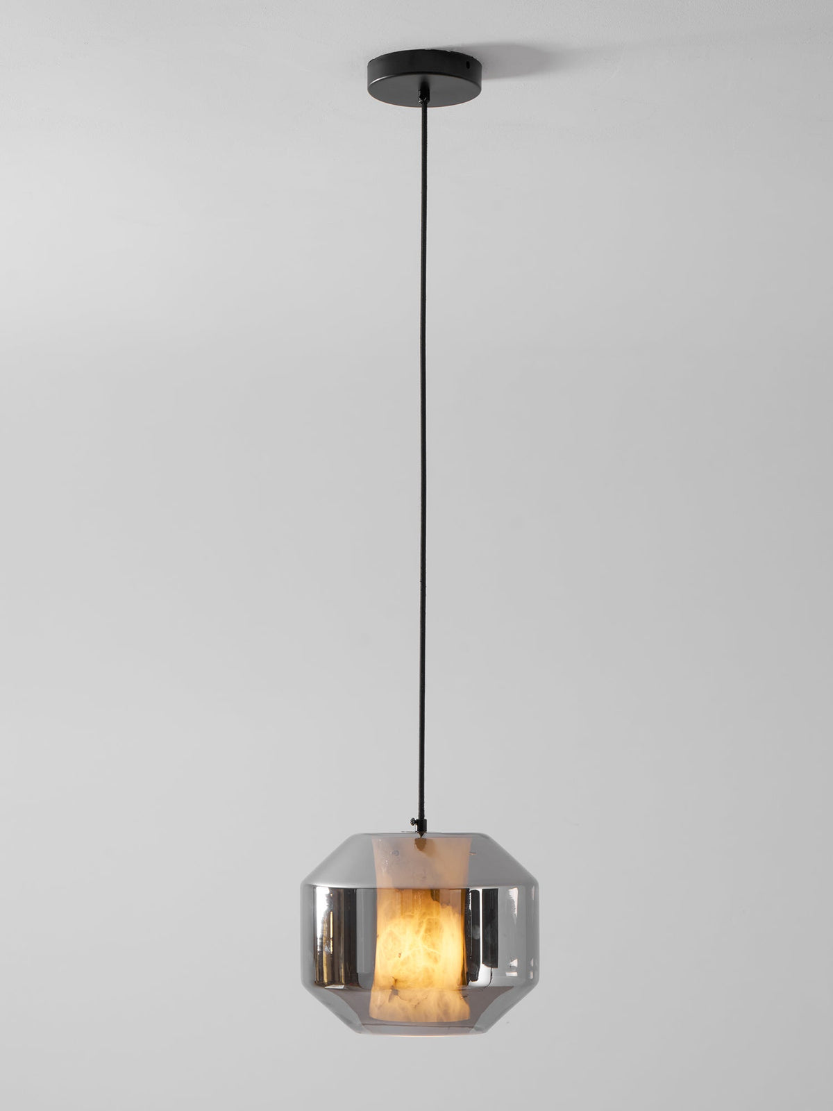 A wide Clérachic pendant on a black cord and canopy, its smoke grey glass shell showing a warm glow from the alabaster inside.