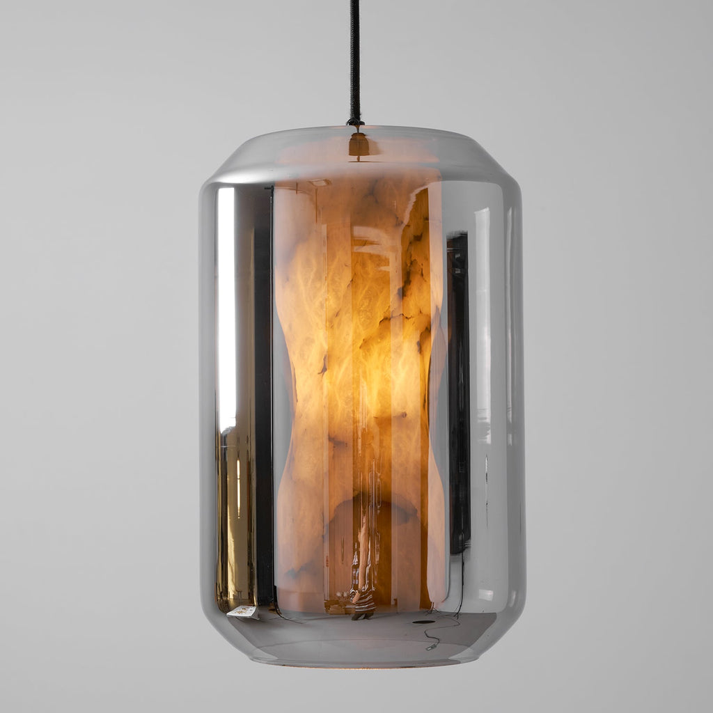 Close view of a tall smoke grey glass Clérachic pendant, its waisted alabaster column glowing amber inside the mirrored shell.