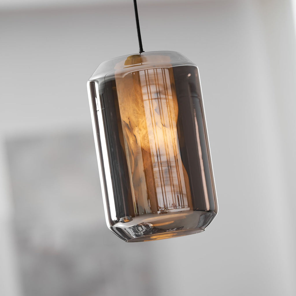 A tall smoke grey glass Clérachic pendant seen at a slight tilt, its alabaster column glowing amber inside the mirrored shell.