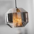 Close view of a wide smoke grey glass Clérachic pendant, the alabaster glowing amber inside against a soft pale blur.