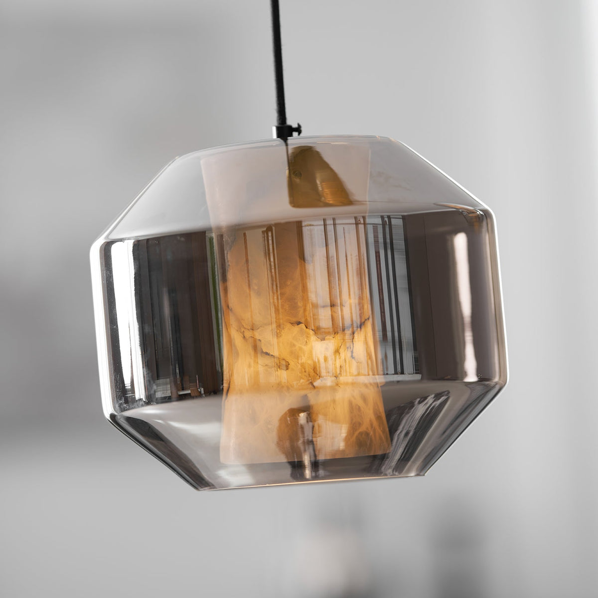 Close view of a wide smoke grey glass Clérachic pendant, the alabaster glowing amber inside against a soft pale blur.