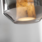 Close view of the rim of a smoke grey glass shell on this Clérachic pendant, with the alabaster column lit warm above it.