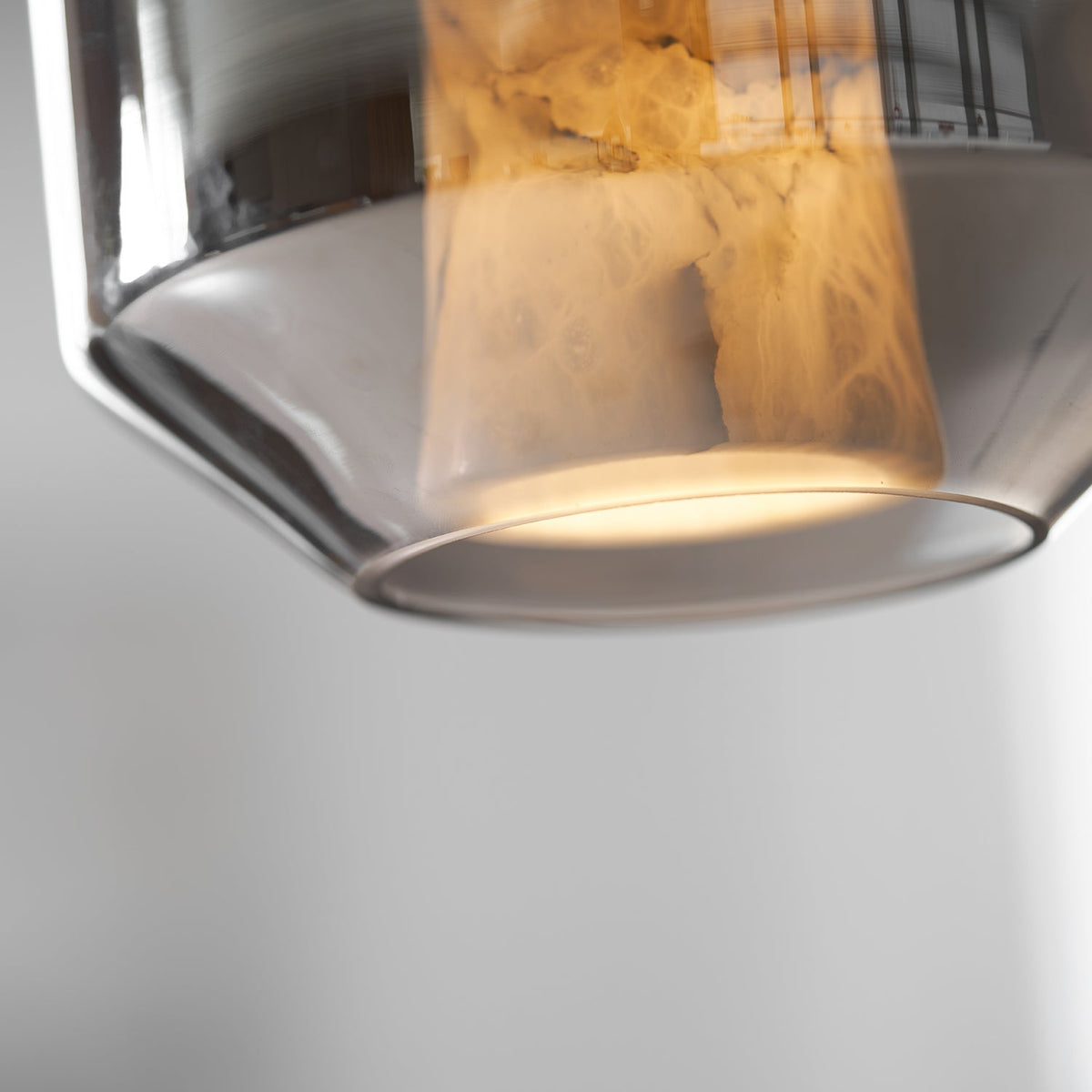 Close view of the rim of a smoke grey glass shell on this Clérachic pendant, with the alabaster column lit warm above it.