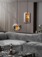 Two smoke grey Clérachic pendants hang above a grey sofa, with a bottle and a glass of whisky on a dark marble table below.