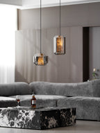 Two small smoke grey Clérachic pendants glow amber in a living room with wood-panelled walls, a grey sofa and a marble coffee table.