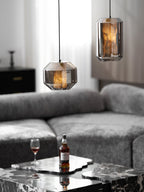 A wide and a tall smoke grey Clérachic pendant glow amber beside sheer curtains, above a grey sofa and a marble table with a whisky glass.