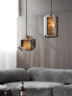 A tall and a wide smoke grey Clérachic pendant hang at different heights above a grey sofa, the tall one lit amber and the wide one dimmer.