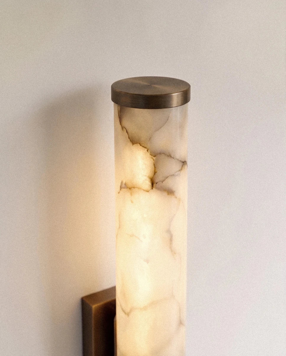 Close view of the Clérachic alabaster wall light's dark metal end cap and glowing cylinder, cloudy veining lit from within.