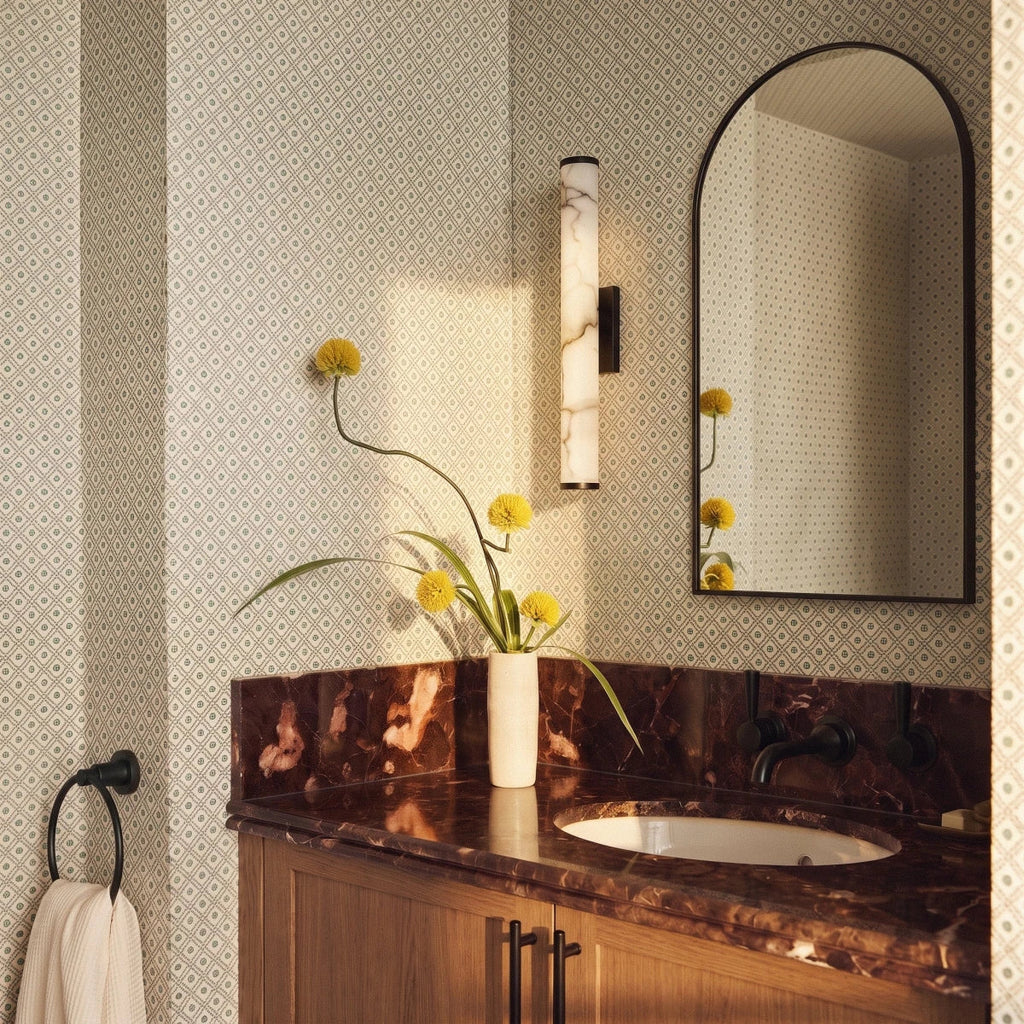 Clérachic alabaster wall light beside an arched black mirror above a wooden vanity with a red marble top and patterned wallpaper.