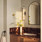 Clérachic alabaster wall light beside an arched black mirror above a wooden vanity with a red marble top and patterned wallpaper.