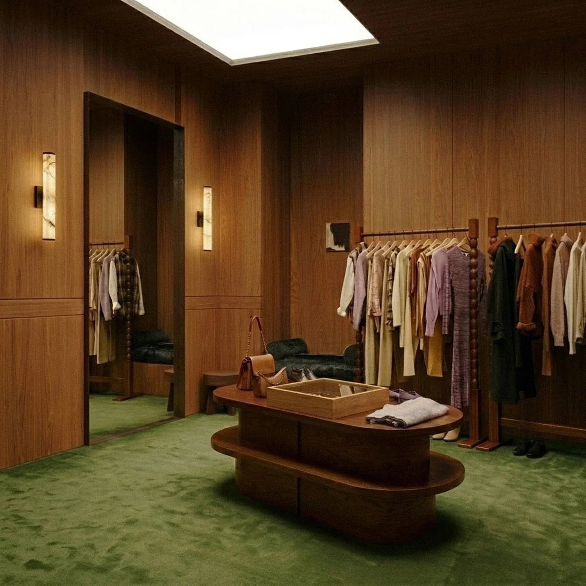 Two Clérachic alabaster wall lights glowing on oak-panelled walls in a walk-in wardrobe with green carpet and a clothing rail.
