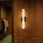 Clérachic alabaster wall light switched on, mounted on oak panelling beside an open wardrobe doorway with hanging clothes.