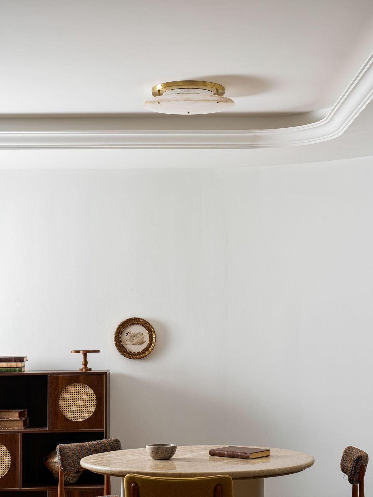 Distant view of a low, unlit Clérachic ceiling disc against a white ceiling edge, with a small round table and a wooden cabinet below.
