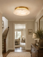 Clérachic alabaster light above a staircase hallway with a wooden console, a leafy plant and a rug leading into the next room.