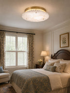 This Clérachic ceiling disc lights a bedroom with floral curtains, a carved wooden headboard and a blue patterned bedspread.