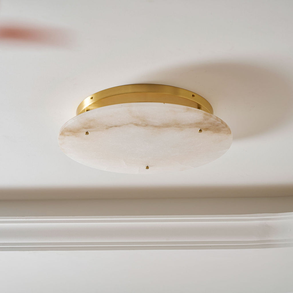 Close view from below of the veined alabaster disc and slim brass canopy on this Clérachic ceiling light, against a white ceiling.