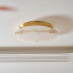 Close view from below of the veined alabaster disc and slim brass canopy on this Clérachic ceiling light, against a white ceiling.