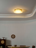 Clérachic disc light glowing warm gold under a ceiling moulding, above a round stone table with a book and a cup.