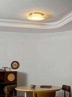 Clérachic flush-mount disc lit warm on a white ceiling, with a round wall ornament and a small table in the room beneath.
