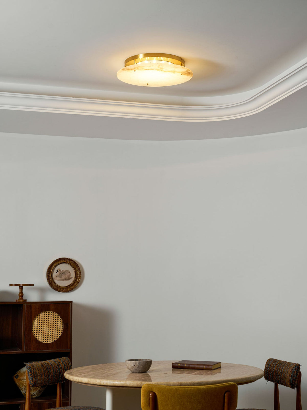 Clérachic flush-mount disc lit warm on a white ceiling, with a round wall ornament and a small table in the room beneath.