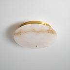 Clérachic alabaster disc mounted on a pale wall, shown from the front, with amber veining and a slim brass band behind.
