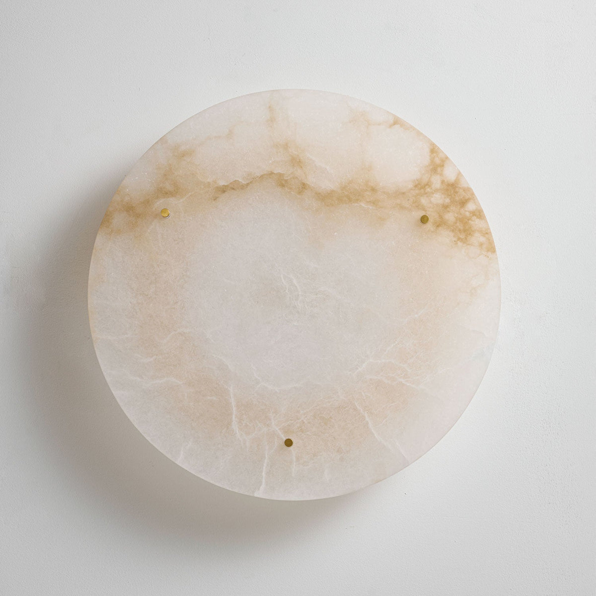 Round Clérachic alabaster disc seen head-on against a white surface, with a band of amber veining and three small brass studs.