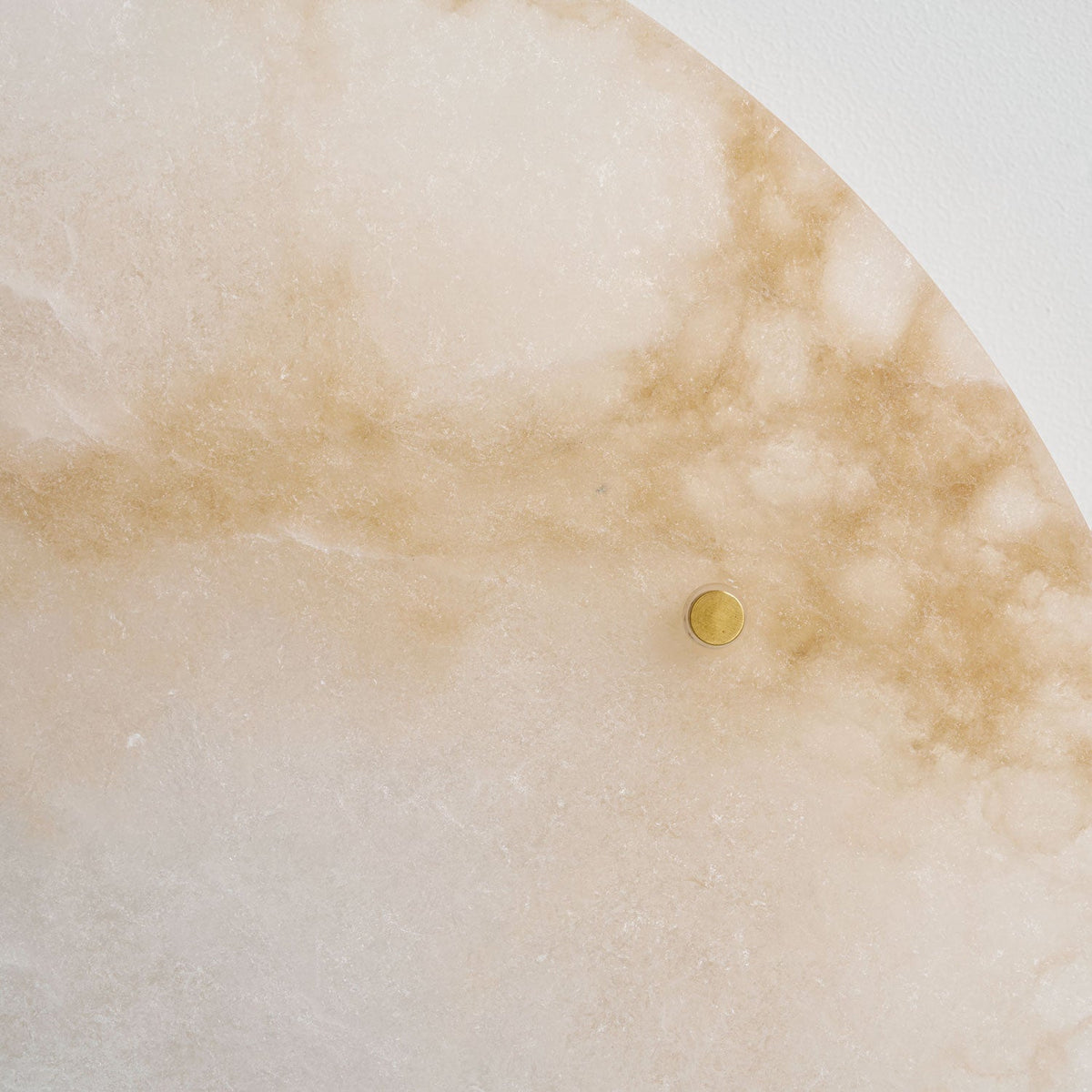 Close-up of the pale, cloudy alabaster on this Clérachic disc light, with amber veins and one brass stud.