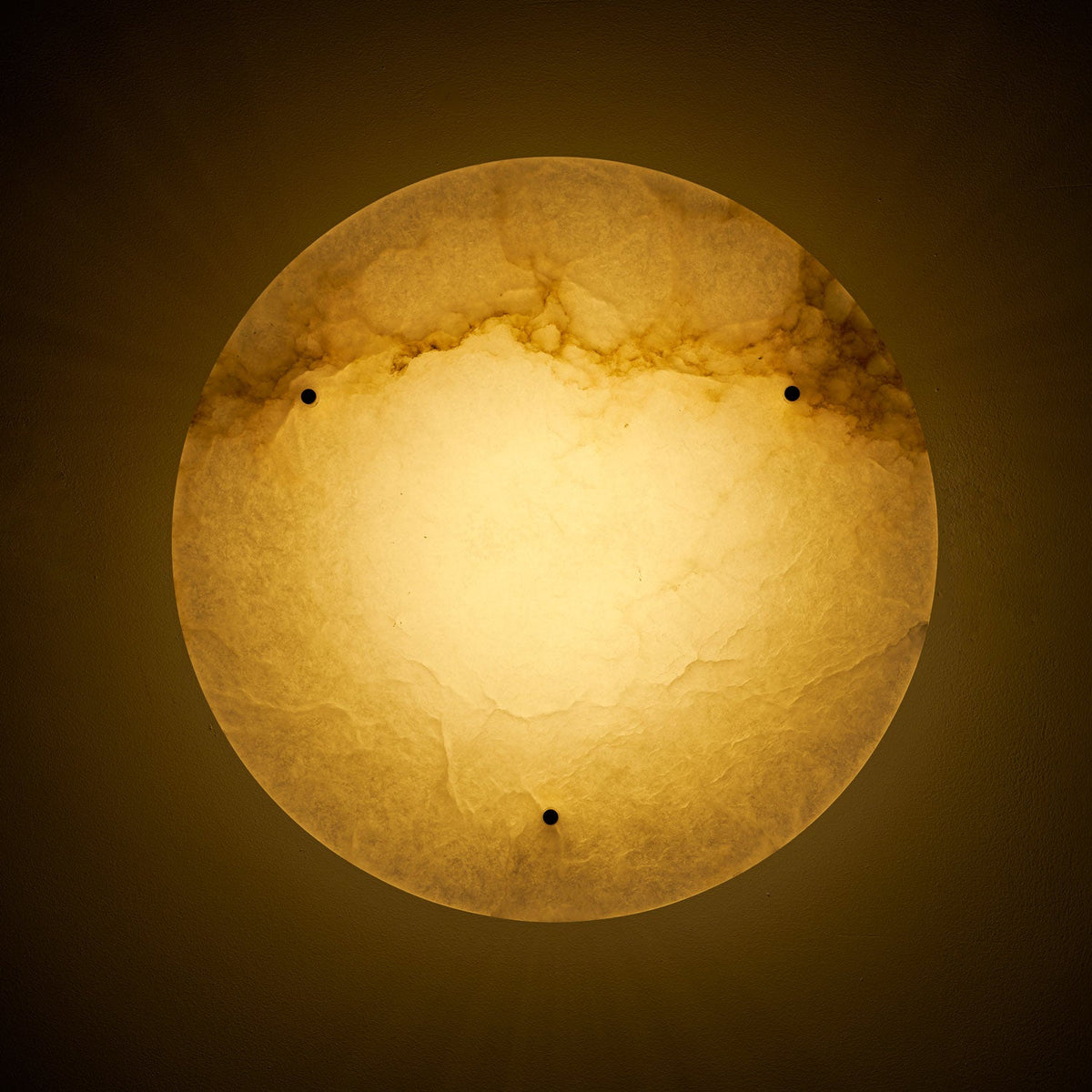 Lit Clérachic alabaster disc seen from below on a dark background, its glow warm gold and the veining showing through.