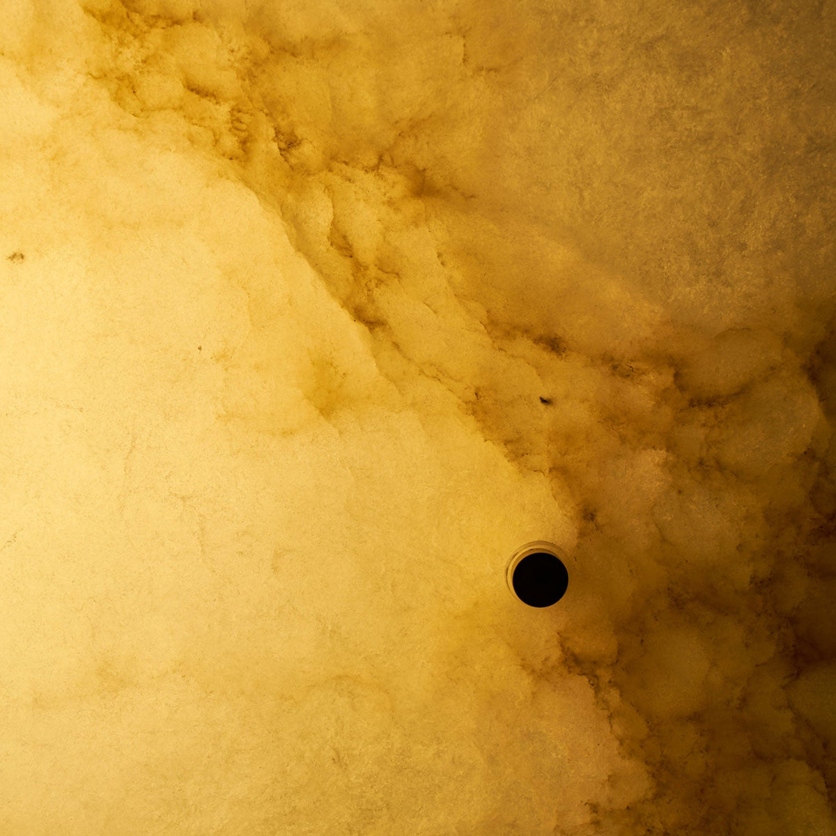 Very close view of the lit alabaster on this Clérachic ceiling light, with golden cloud-like veins and a dark screw hole.