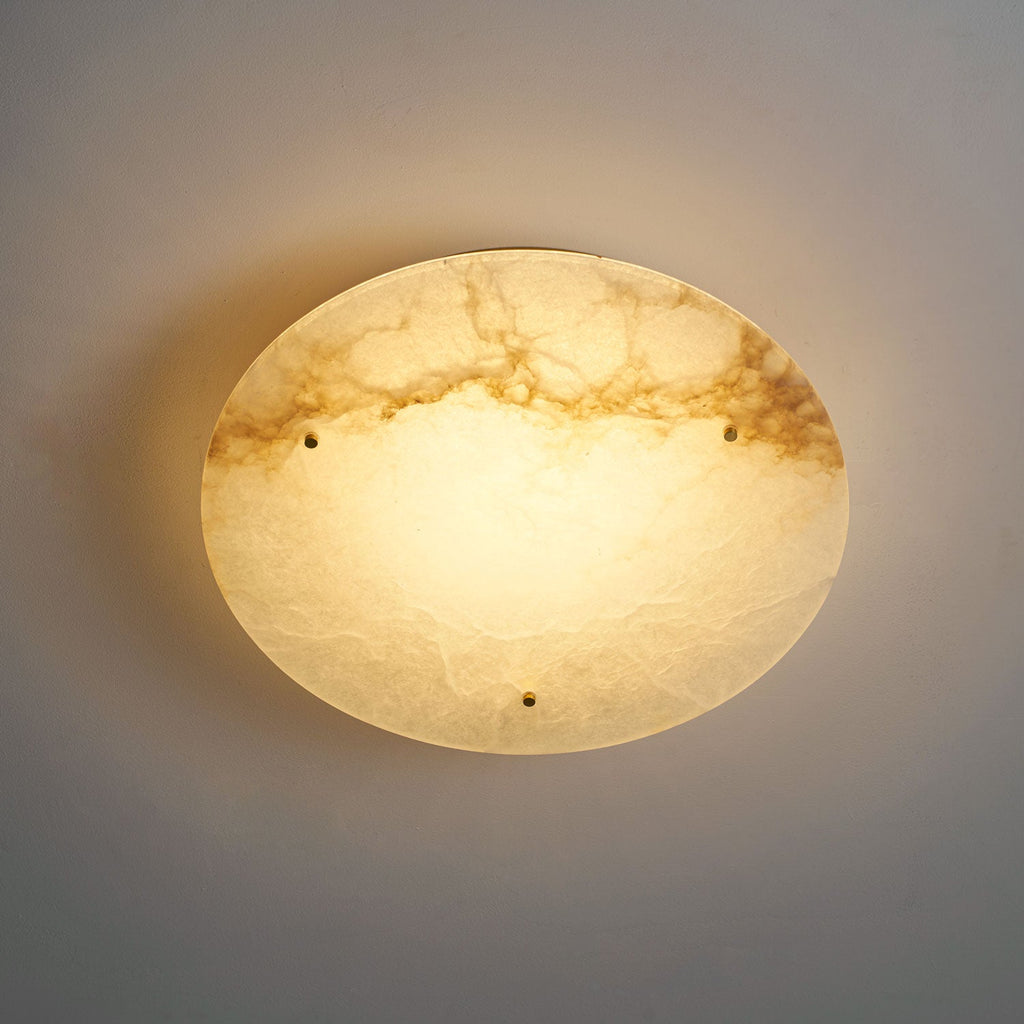 Clérachic alabaster disc glowing warm from below on a grey ceiling, with soft light spilling onto the surface around it.