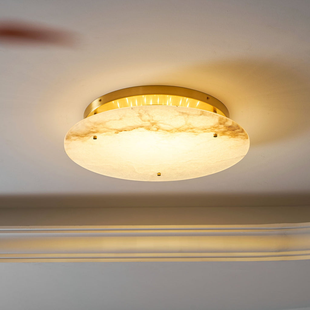Side view of the Clérachic alabaster disc switched on, its brass ring glowing above a ceiling edge and a glass shelf below.