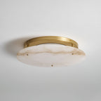 Clérachic flush-mount alabaster disc with a brass canopy, unlit, mounted on a pale grey ceiling and seen from one side.