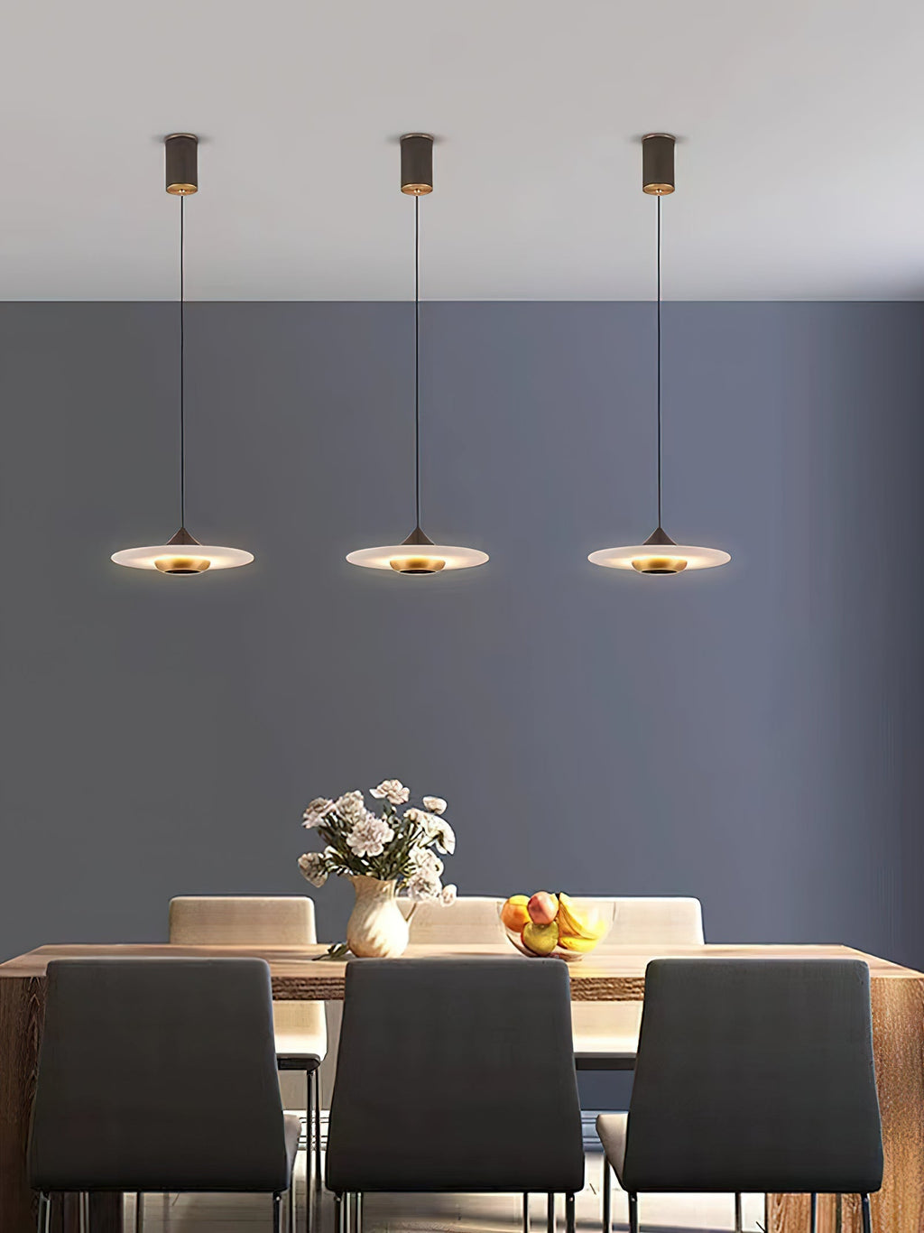 Three Clérachic Alabaster Disc Pendant Lights hung in a row above a wooden dining table against a deep grey wall.