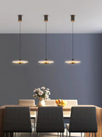 Three Clérachic Alabaster Disc Pendant Lights hung in a row above a wooden dining table against a deep grey wall.
