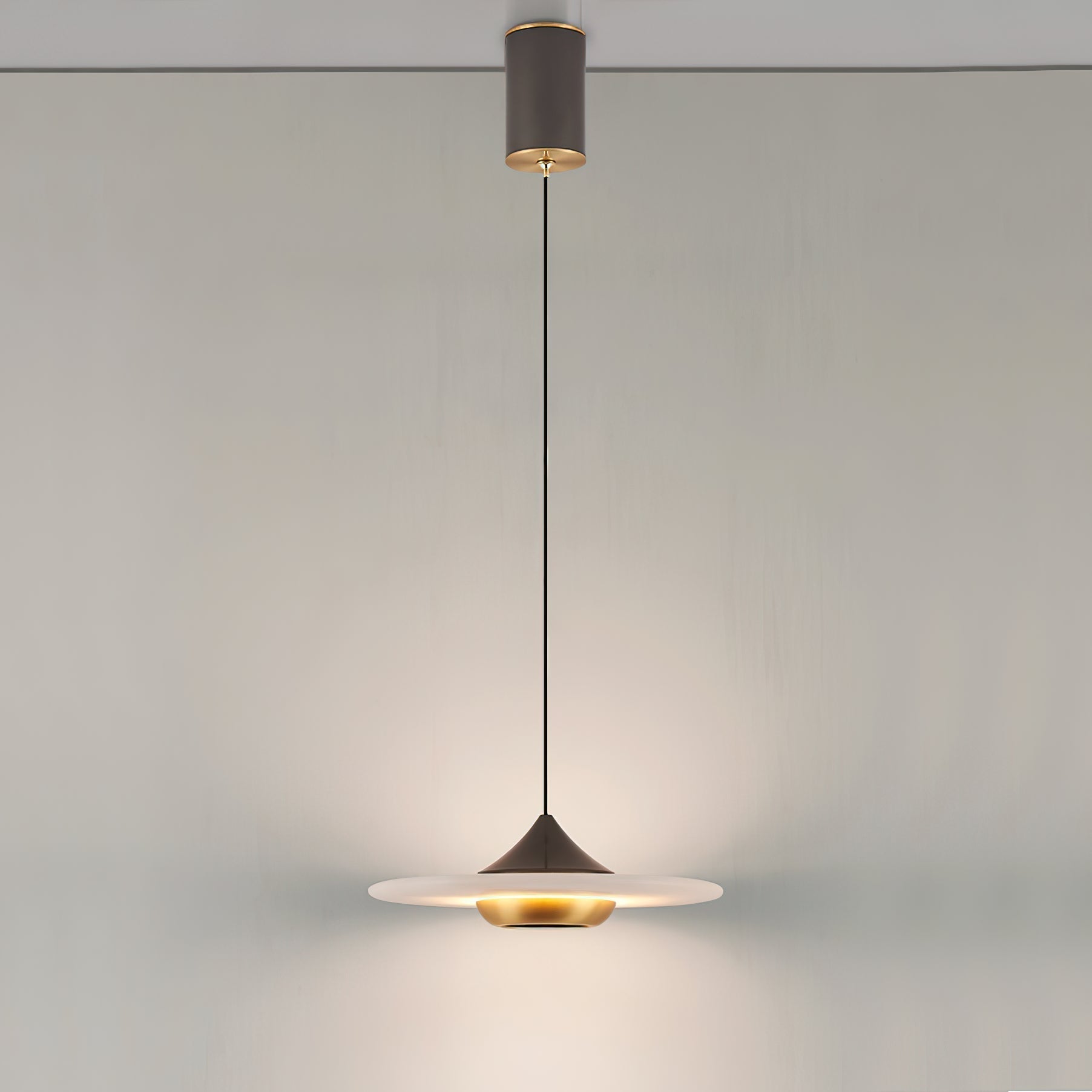 Clérachic Alabaster Disc Pendant Light hung from its cylindrical ceiling canopy, lighting a plain wall from a long drop.