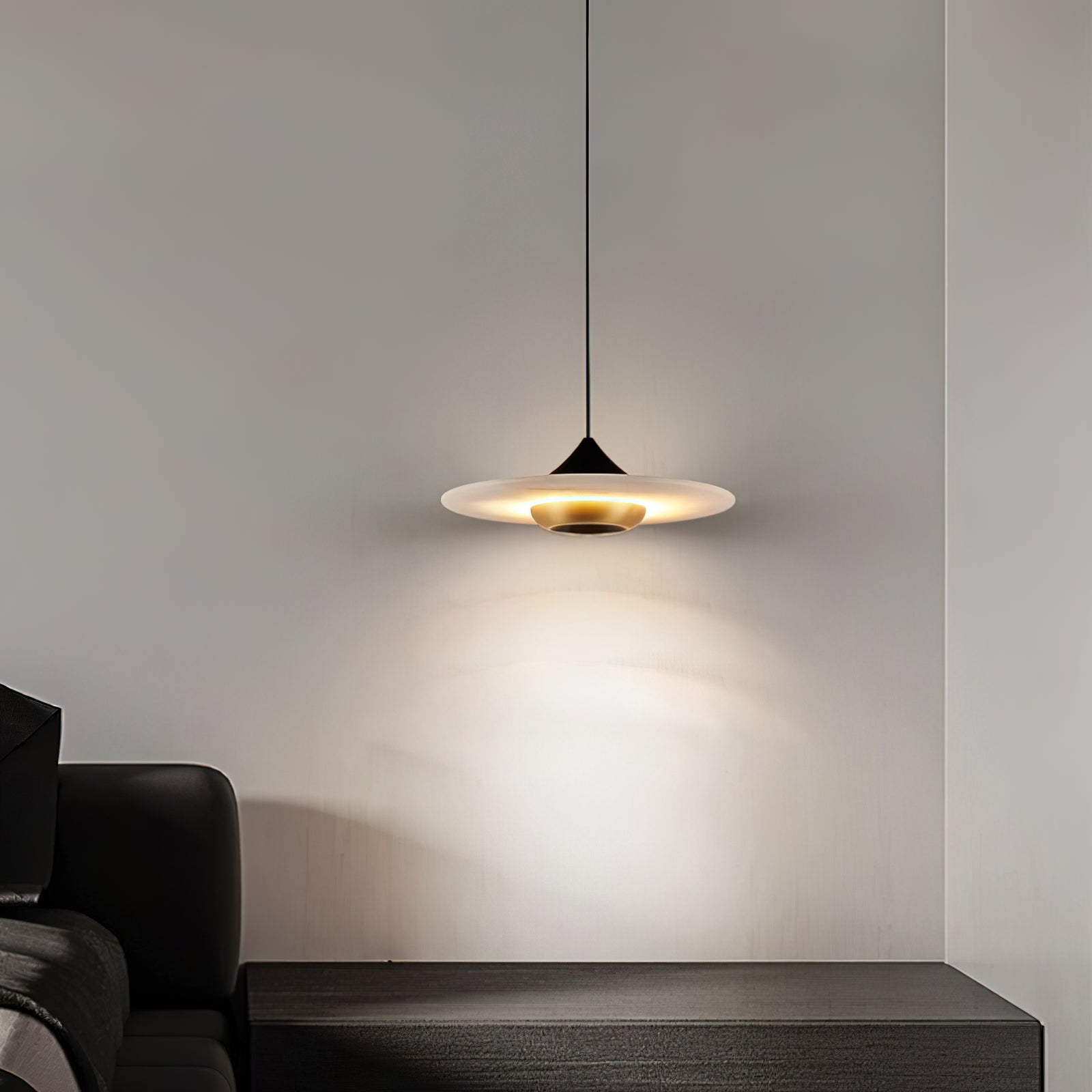 Clérachic Alabaster Disc Pendant Light above a dark wood console, a warm halo of light on the bedroom wall behind it.