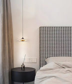 Clérachic Alabaster Disc Pendant Light hung low beside a houndstooth headboard, lighting a round black bedside table.