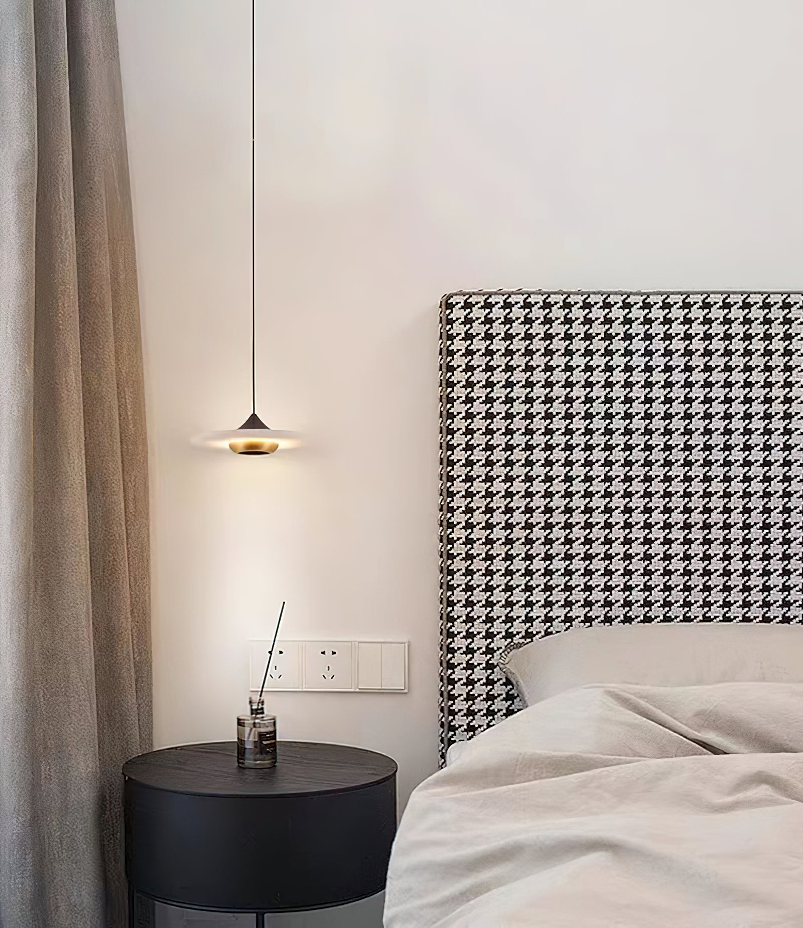 Clérachic Alabaster Disc Pendant Light hung low beside a houndstooth headboard, lighting a round black bedside table.