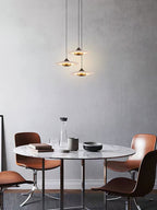 Three Clérachic Alabaster Disc Pendant Lights staggered at different drops over a round marble dining table.